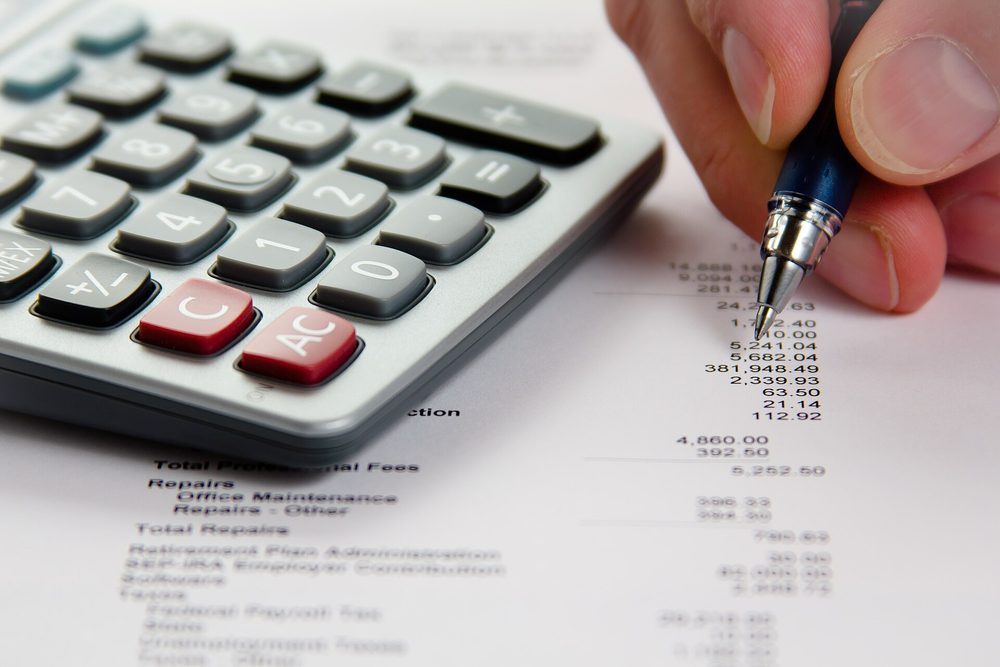 A hand working through a printed financial statement with a calculator